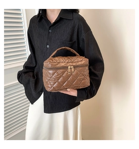 Close-up of quilted brown vanity bag with gold dual zippers and top handle details