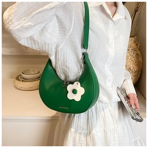 Detail of green hobo bag featuring smooth leather and a white floral pendant accessory