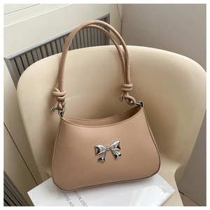 Detail of a beige handbag featuring a silver bow accent and stylish twisted shoulder strap