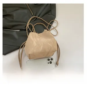 Top view of beige drawstring bucket bag with gold chain strap next to a smartphone