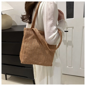 Dettaglio di una borsa tote in paglia marrone con trama a V e tracolla lunga in primo piano