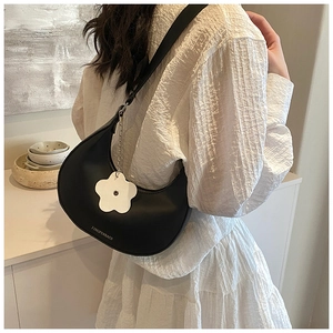 Detail of black leather hobo bag featuring a white flower charm and smooth curved design