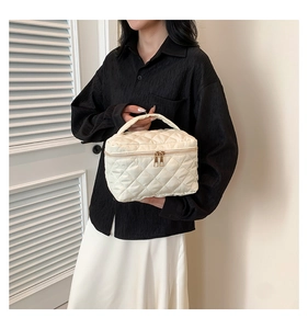 Quilted off-white mini box bag with top handle and gold zipper shown on a model