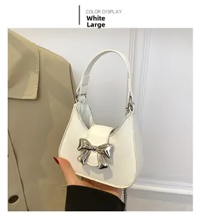 Close-up of a white textured handbag with a silver metal bow and integrated handle detail