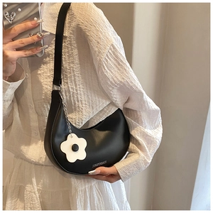 Close-up of black crescent saddle bag on model with white flower charm and branding