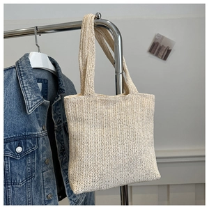 Dettaglio della borsa in paglia intrecciata beige appesa accanto a una giacca di jeans