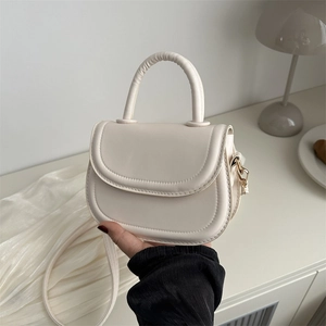 Cream white mini saddle bag with top handle and gold hardware shown in lifestyle scene