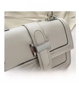 Detail of white PU leather crossbody bag with black contrast stitching and silver metal buckle