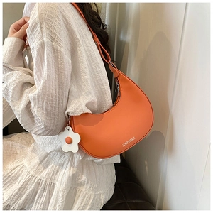 Orange crescent moon shoulder bag featuring a knotted strap and a floral charm detail