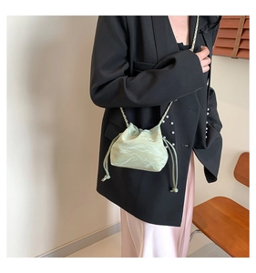 Detail of light green drawstring bucket bag with glossy pleated texture on model