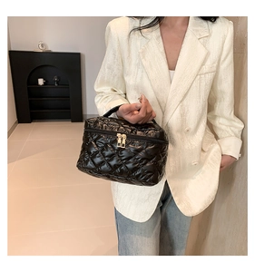 Detail of black quilted box handbag featuring a shiny finish and golden dual zippers