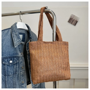 Dettaglio della trama intrecciata e dei doppi manici di una borsa tote in paglia marrone