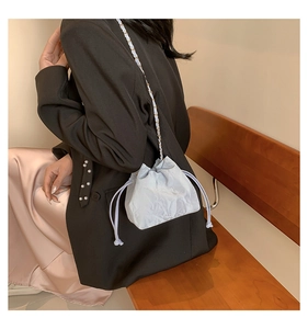 Detail of light blue pleated bucket bag featuring woven gold chain and drawstring closure