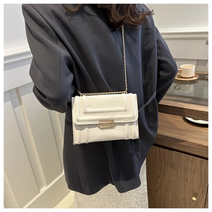 Detail of cream glossy faux leather crossbody bag featuring embossed texture and gold chain