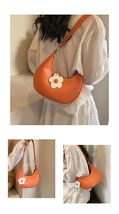 Close-up of orange crescent saddle bag with white floral charm and logo detail