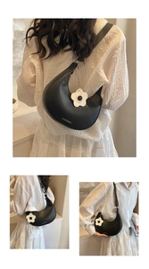 Detail of black crescent shoulder bag with white flower charm and brand logo
