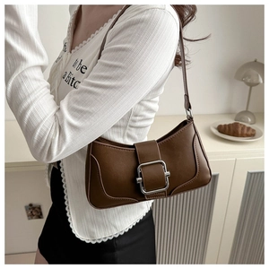 Detail of a dark brown baguette bag with a silver buckle worn as a shoulder bag
