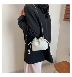 Detail of a white marble pattern drawstring bucket bag with golden chain strap on model