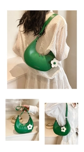 Detail of green crescent saddle bag with floral charm and adjustable shoulder strap