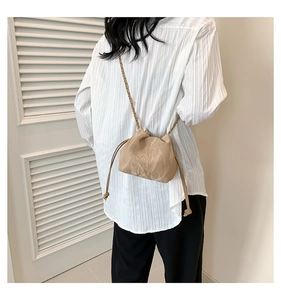 Detail of a beige pleated drawstring crossbody bag with a metal chain strap on a model
