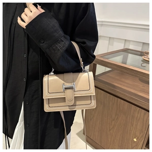 Detail view of stylish beige square bag featuring silver lock and decorative wave stitching