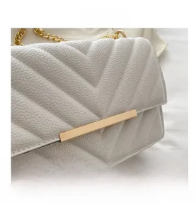 Close-up of white lychee leather bag with V-shaped quilting and gold metal chain