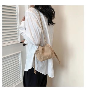 Detail of beige pleated bucket bag with gold chain strap shown on model's shoulder