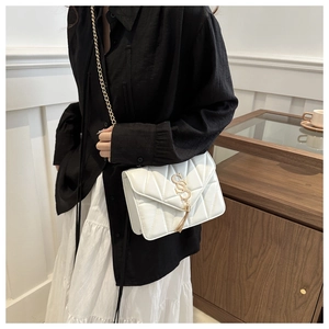 Detail of white quilted crossbody bag featuring a gold chain strap and tassel charm