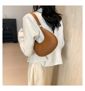 Détail d'un sac porté épaule croissant marron avec boucle dorée porté par un mannequin