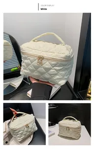 Detailed view of white quilted cosmetic bag featuring gold double zippers and top handle