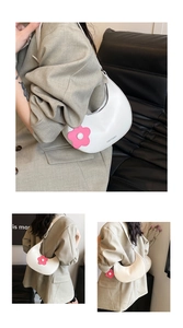 Detail of white crescent saddle bag with a pink floral charm and smooth faux leather finish