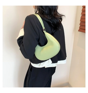 Gros plan d'un sac sous le bras croissant vert clair porté avec un blazer noir chic