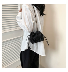 Detail of black drawstring bucket bag featuring embossed texture and chain shoulder strap