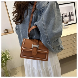 Brown leather crossbody bag detail featuring white stitching and silver metal buckle