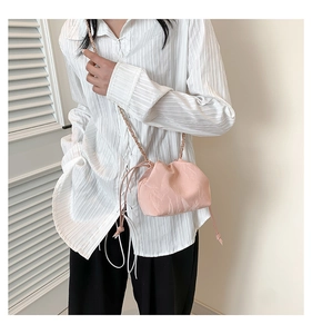 Detail of soft pink pleated bucket bag with metal chain strap worn by a female model
