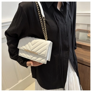 Close-up of white chevron quilted chain crossbody bag worn by a model in casual setting