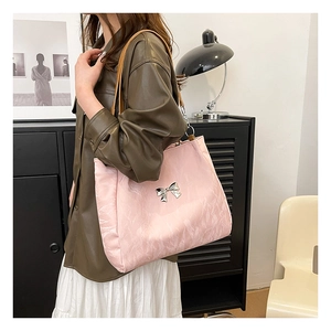Detail of light pink tote bag with silver butterfly emblem and brown leather strap