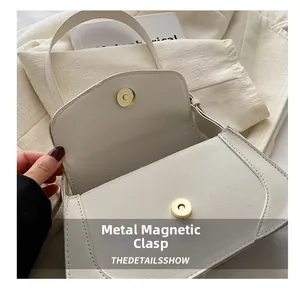 Close-up of golden magnetic hardware clasp on cream pebbled leather shoulder bag