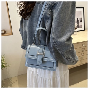 Detail of light blue crossbody bag featuring contrast black and white stitching on the edges