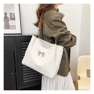 Detail of white velvet tote bag featuring a silver metal butterfly bow and chain strap