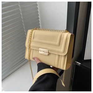 Detail of a creamy yellow crossbody bag featuring geometric embossed lines and gold chain