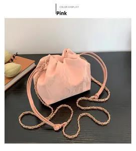 Pink soft leather drawstring bucket bag with gold chain strap on wooden surface