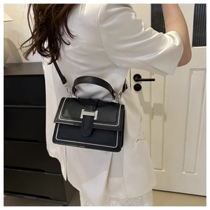 Close-up of black crossbody bag featuring contrasting white stitching and silver buckle