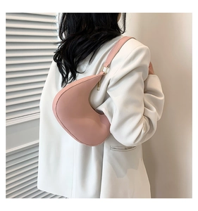 Sac à bandoulière demi-lune rose en similicuir lisse porté sur l'épaule du modèle