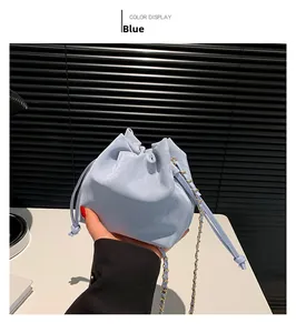 Blue drawstring bucket bag with gold chain strap detail held by a model