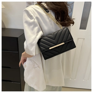 Detail of black chevron quilted leather crossbody bag with gold chain strap on model