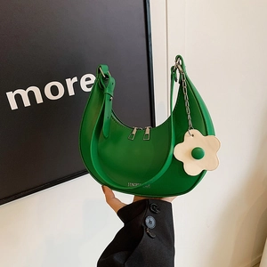 Chic green half-moon saddle bag with white flower charm held against a white wall