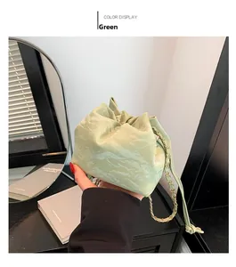 Detail of light green drawstring bucket bag with pleated texture and golden chain strap