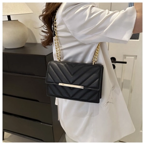 Detail of black quilted shoulder bag featuring gold chain strap and lychee texture faux leather