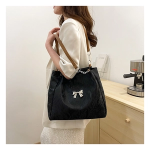 Close-up of black pleated tote bag featuring a silver metal bow and leather chain strap